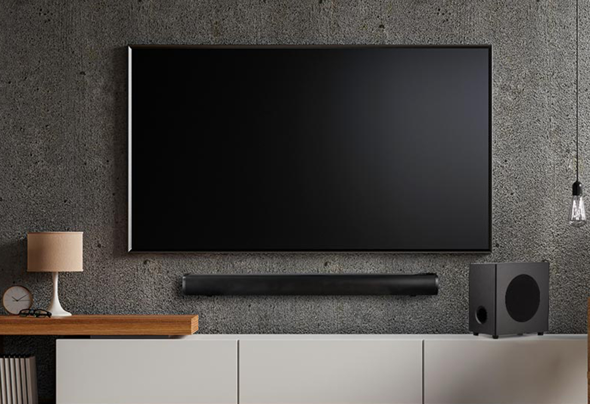 απεικονίζεται μια ηχόμπαρα και ένα subwoofer τοποθετημένα πάνω σε ένα έπιπλο τηλεόρασης
